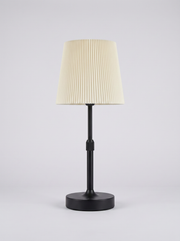Black cordless table lamp with pleated cream shade on a clean studio background