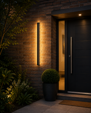 Ealing linear outdoor wall light glowing on brick beside a modern UK front door at dusk