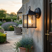 Dulwich Black Lantern Outdoor Wall Light with exposed bulb mounted beside a front door, garden patio in background