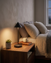 Black cordless table lamp glowing on a bedside table in a warm bedroom