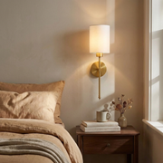 Brass wall light above a bedside table in a warm bedroom