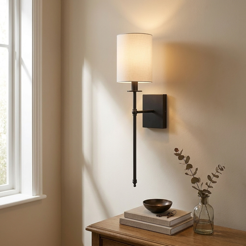 Black candlestick-style wall light with white fabric shade beside a console table, warm glow