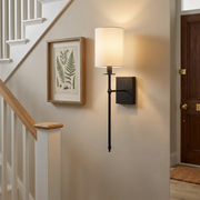 Black candlestick-style wall light beside a staircase landing, warm hallway glow