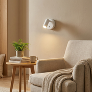 White pivoting wall light beside a reading armchair, warm living room glow