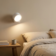 Round magnetic wall light glowing above a bedside table in a warm bedroom