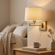 Gold swing-arm wall light glowing above a bedside table