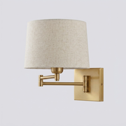 Gold swing-arm wall light with linen drum shade on plain background