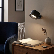 Black rotatable wall light glowing above a reading corner console table