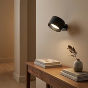 Black rotatable wall light beside books and a vase in a hallway