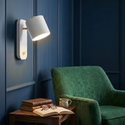 White rotatable cone wall light glowing in a reading corner