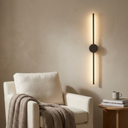 Dark linear wall light glowing beside a reading chair