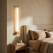 Slim vertical linear wall light glowing beside a bed
