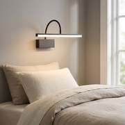 Black battery wall light glowing on a bedroom wall beside the bed