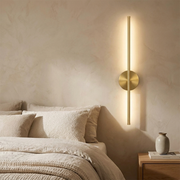 Battery wall light glowing warmly on a bedroom wall beside a bed