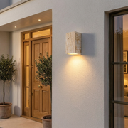 Travertine outdoor wall light glowing beside a front entrance at dusk