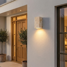 Travertine outdoor wall light glowing beside a front entrance at dusk