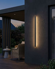 Black linear outdoor wall light glowing on a patio wall at dusk