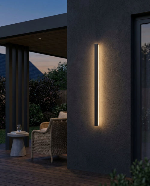 Black linear outdoor wall light glowing on a patio wall at dusk