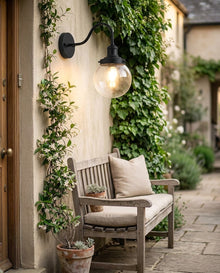 Black gooseneck outdoor wall light with glass globe beside a cottage door