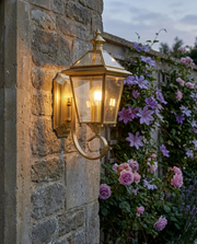 Brass lantern outdoor wall light glowing on a garden wall beside climbing roses
