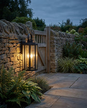 Black metal lantern outdoor wall light on a garden boundary wall at dusk