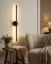 Black rotatable linear wall light beside a reading armchair with warm ambient glow