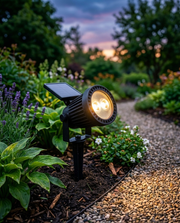 Solar garden spike spotlight lighting a flower border along a gravel path