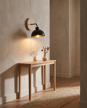 Black dome wall light with wood backplate warming a hallway console table
