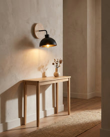 Black dome wall light with wood backplate warming a hallway console table