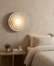 Round ribbed resin wall light glowing warmly beside a bedside table