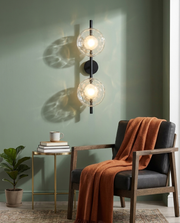 Black double-globe wireless wall sconce glowing softly in a living room corner