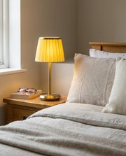 Gold cordless table lamp with pleated fabric shade glowing on a bedside table