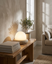 Cream travertine dome table lamp glowing on a console table beside a window