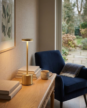 Gold cordless table lamp with disc shade glowing on a console table