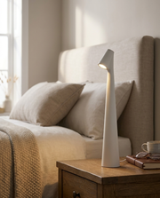 White cordless table lamp glowing on a bedside table in a warm bedroom