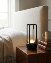 Black cordless lantern table lamp glowing on a walnut bedside table