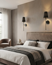 Black battery wall light pair beside a bed creating warm symmetrical bedside light