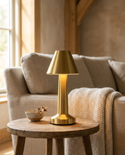 Gold cordless table lamp glowing on a side table beside a living room sofa
