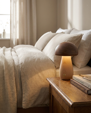 Wood mushroom cordless table lamp glowing on a bedside table