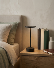 Black cordless metal table lamp glowing on a wooden bedside table