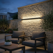 Ealing Long IP65 Linear Outdoor Wall Light - Black, mounted on a stone garden wall at dusk