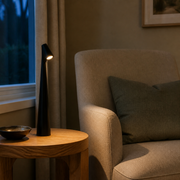 Leighton black cordless table lamp providing warm reading light beside an armchair