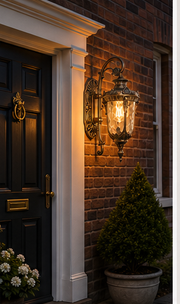 Bronze Notting glass lantern glowing on a stone cottage wall beside the front door at dusk