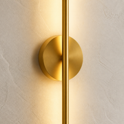 Close-up of the Stamford gold wall light's slim vertical bar, round wall plate and brushed finish