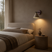 Stratford travertine cone wall light casting a warm downward glow beside a neutral bed