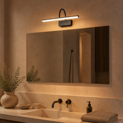 Walton black linear battery wall light illuminating a wide mirror in a warm stone vanity area