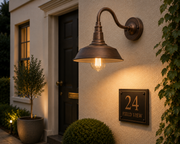 Bronze gold Wren gooseneck outdoor light glowing beside a UK cottage front door at dusk